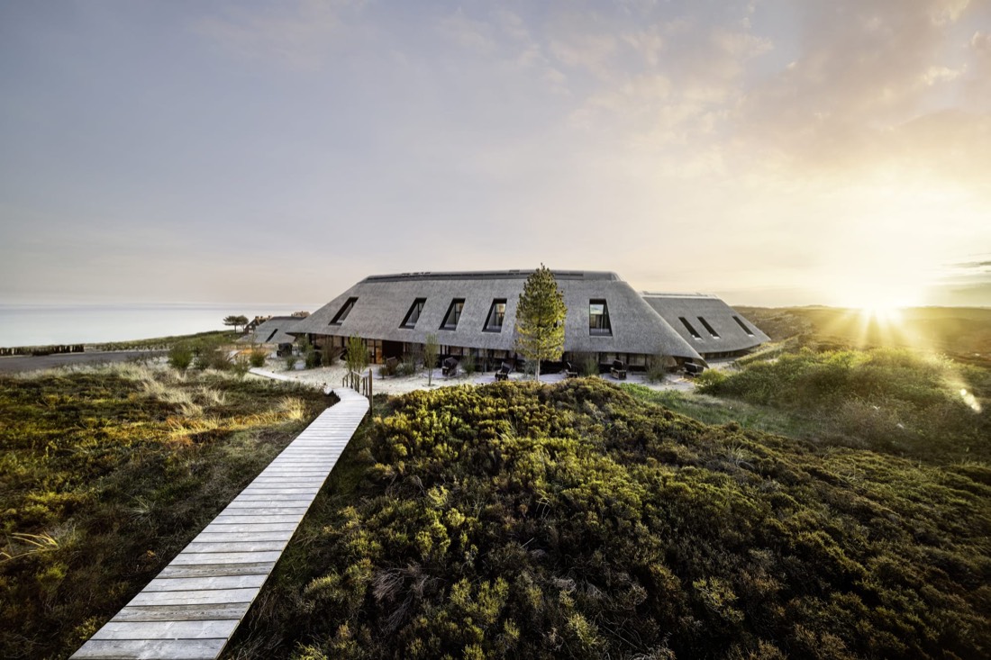 Edificio de Lanserhof Sylt entre dunas, con pasarela de madera al amanecer